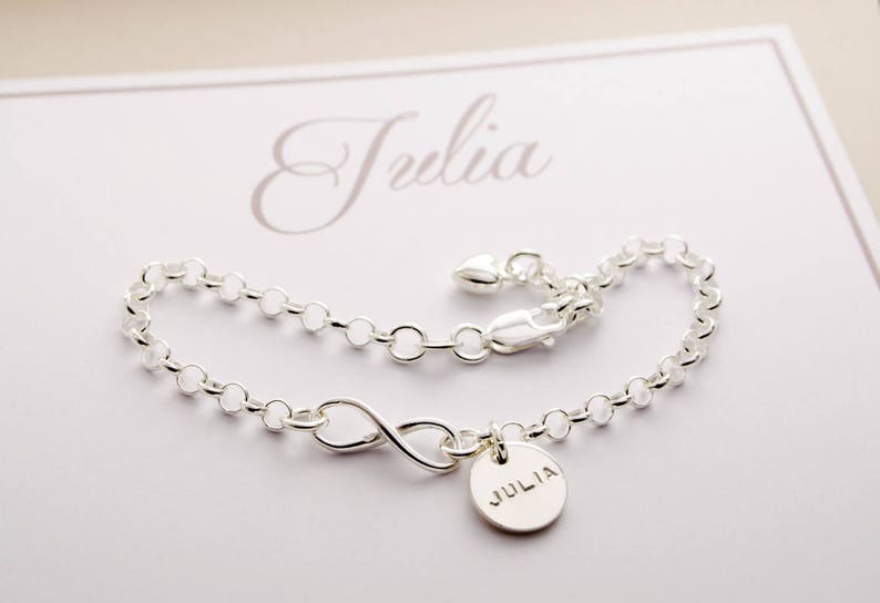May include: Silver infinity charm bracelet with a personalized name tag that reads "Julia".
