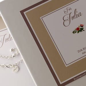 May include: A white gift box with a brown border and the text "F&uuml;r Julia Zur Kommunion am 30.04.2017" and the text "BLOOMGART ACCESSOIRES". A silver bracelet with a charm that says "Julia" is on the box.