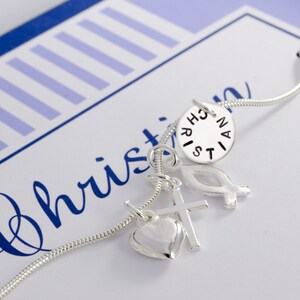May include: Silver necklace with charms including a heart, cross, fish, and a round charm with the word "Christian" inscribed on it.