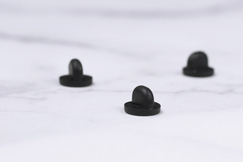 May include: Close-up of three small, black, mushroom-shaped objects. Each object has a rounded top and a flat, circular base. The objects are evenly spaced against a white background.