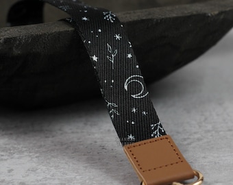 May include: Black and white patterned lanyard with a brown leather strap and a gold metal clip. The pattern features stars, moons, and leaves.