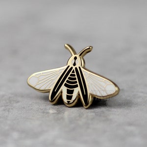 May include: Gold-tone enamel pin featuring a black and white bee design. The bee has a white body with black stripes and wings. The pin is a great addition to any insect lover's collection.