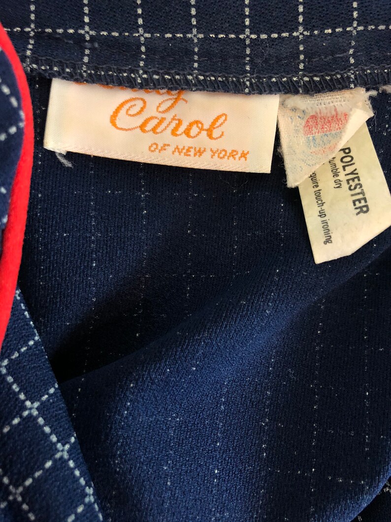 May include: A navy blue checked fabric with a white label that reads "Lady Carol of New York" and a white label that reads "Polyester, tumble dry, require touch-up ironing".