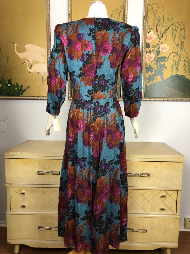 May include: A long, blue dress with a floral print featuring pink, purple, and brown flowers. The dress has a v-neck and long sleeves.