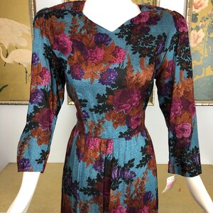 May include: A long-sleeved dress with a floral print in shades of blue, purple, brown, and black. The dress has a v-neck and a fitted bodice. The skirt is full and flowing.
