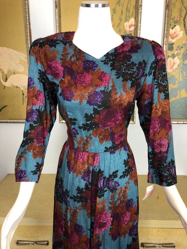 May include: A long-sleeved dress with a floral print in shades of blue, purple, brown, and black. The dress has a v-neck and a fitted bodice. The skirt is full and flowing.