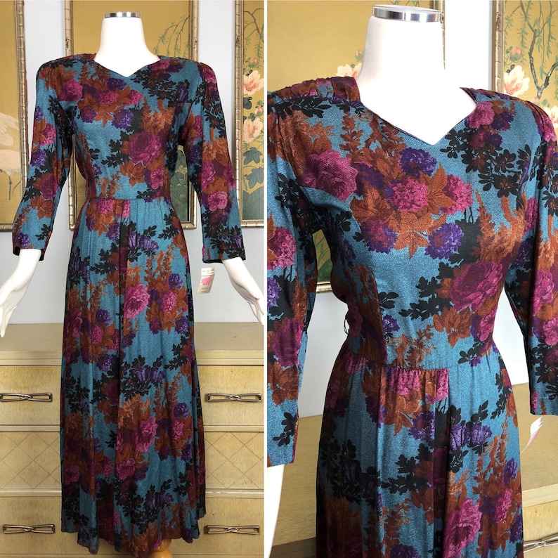 May include: A teal blue maxi dress with a floral print featuring shades of purple, brown, and black. The dress has a V-neckline and 3/4 sleeves.