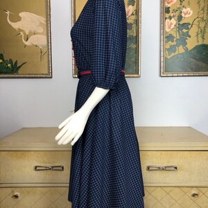 May include: A navy blue and white gingham dress with red trim around the collar and waist. The dress has a fitted bodice and a full skirt.