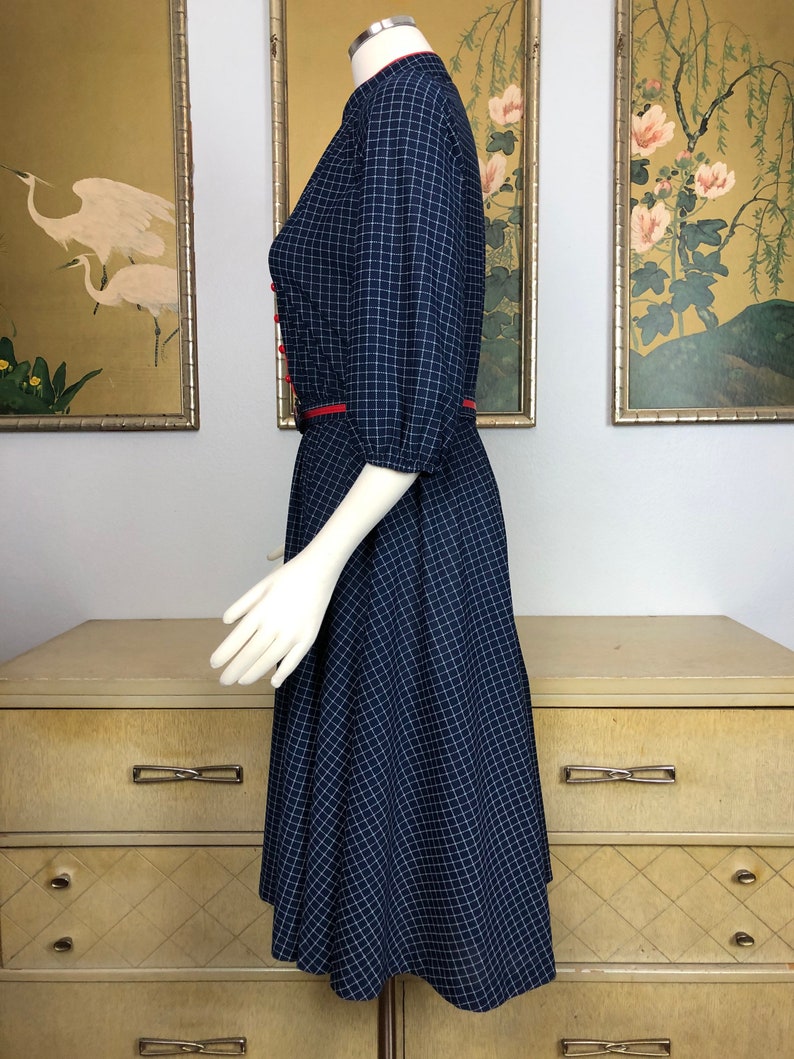 May include: A navy blue and white gingham dress with red trim around the collar and waist. The dress has a fitted bodice and a full skirt.
