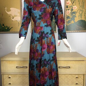 May include: A long, teal blue dress with a floral print in shades of purple, brown, and black. The dress has a v-neckline and 3/4 sleeves.
