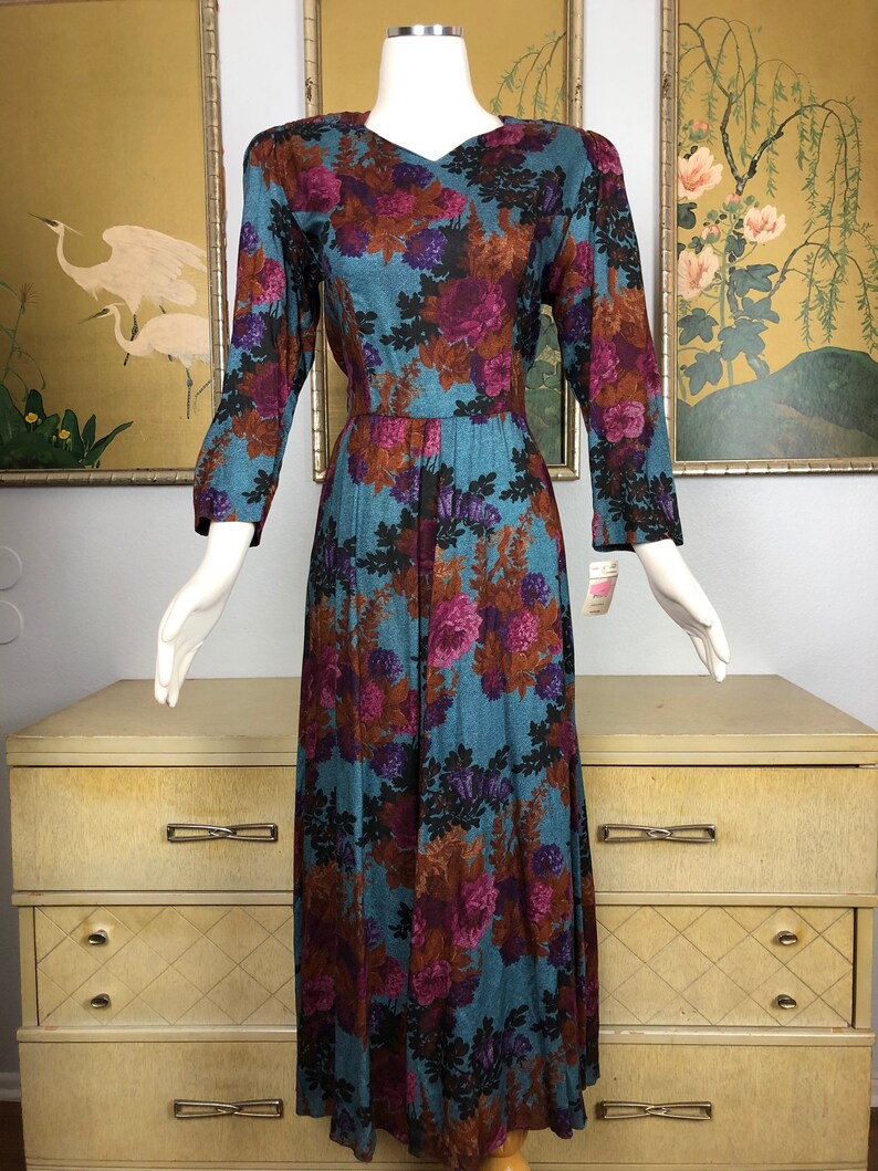 May include: A long, teal blue dress with a floral print in shades of purple, brown, and black. The dress has a v-neckline and 3/4 sleeves.