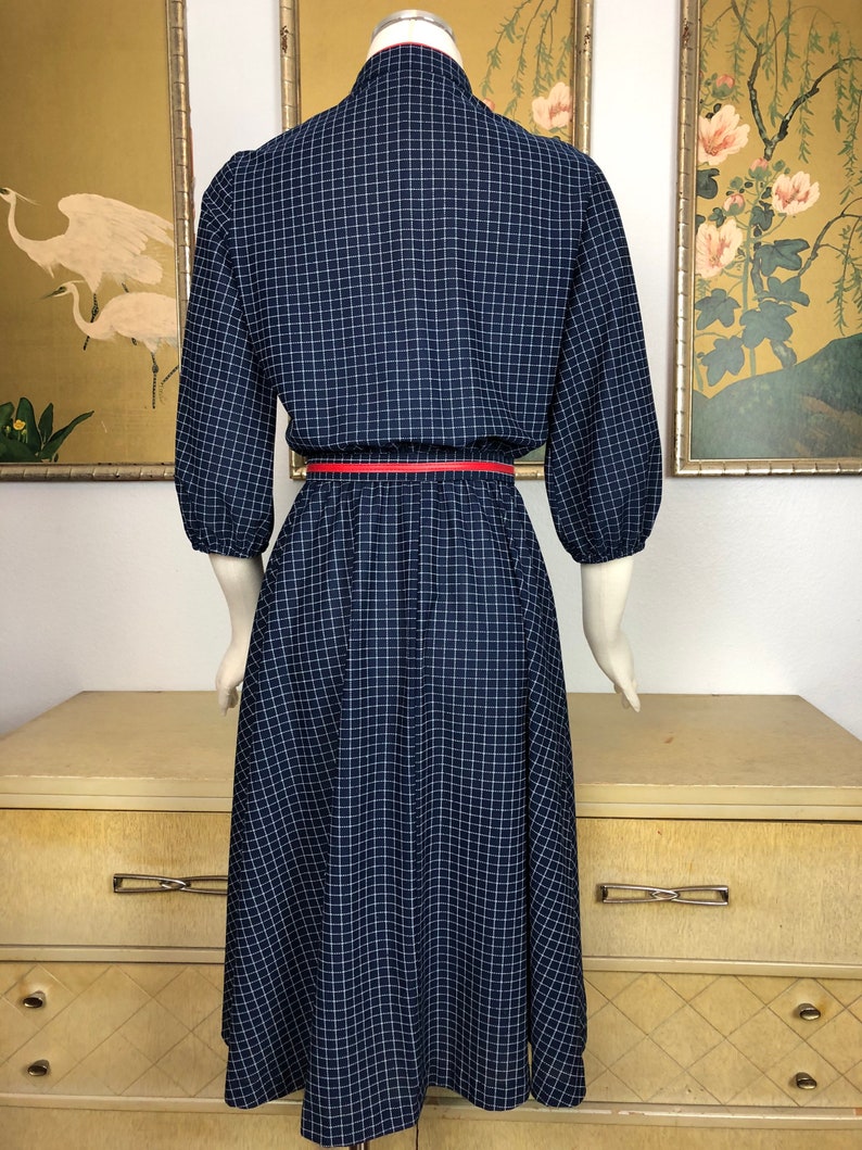 May include: A navy blue and white gingham dress with a red belt. The dress has a collared neckline and 3/4 sleeves.
