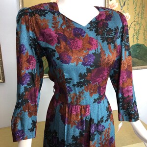May include: A long-sleeved dress with a floral print in shades of brown, purple, and black on a teal blue background. The dress has a v-neck and a fitted bodice.