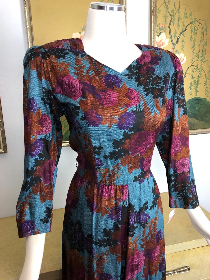 May include: A long-sleeved dress with a floral print in shades of brown, purple, and black on a teal blue background. The dress has a v-neck and a fitted bodice.