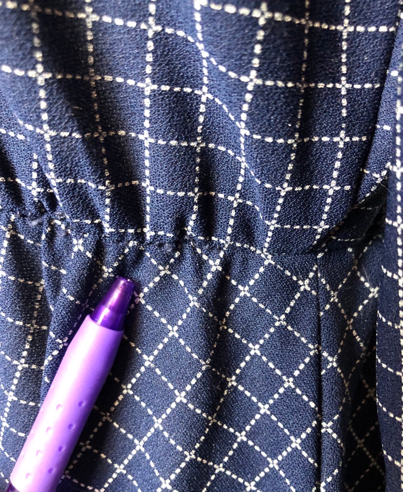 May include: Close-up of a navy blue fabric with a white grid pattern. The fabric has a slight texture and is slightly wrinkled.