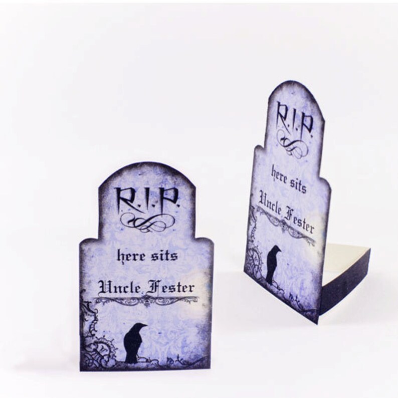 Puede incluir: Dos tarjetas de lugar de Halloween en forma de l&aacute;pida, de color morado y negro, con el texto "R.I.P. here sits Uncle Fester" y una ilustraci&oacute;n de cuervo negro.
