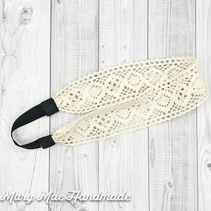 May include: A white crocheted headband with a black elastic band. The headband is on a white wooden background.