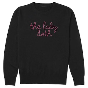 Könnte beinhalten: Schwarzer Rundhals-Pullover mit dem in Rosa gestickten Text "the lady doth". Der Pullover hat lange Ärmel und ein schlichtes Design, geeignet für den Alltag.