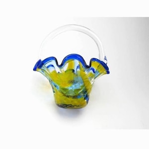 May include: A decorative glass basket with a clear handle and a ruffled rim. The basket features a vibrant color scheme of yellow, blue, and green, with a clear glass handle. The rim is trimmed with a deep blue.