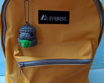 May include: Mustard yellow backpack with a front pocket and a gray zipper. A small, crocheted gray and green creature charm hangs from the zipper. The brand name "EVEREST" is printed on a black rectangle.