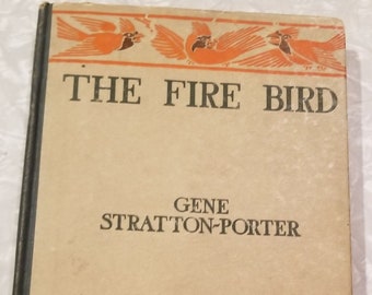 May include: The cover of a vintage book titled "The Fire Bird" by Gene Stratton-Porter. The cover features a decorative border with orange birds and white flowers.