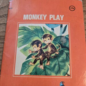 May include: A vintage children's book titled "Monkey Play" with an illustration of two monkeys on a leafy branch. The book is published by A Rand McNally Tiny Elf.