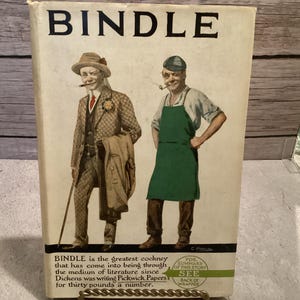 Puede incluir: Portada de libro vintage titulada "BINDLE" con ilustraciones de dos hombres, uno con traje y sombrero, el otro con delantal. La portada incluye texto que describe el contenido del libro y una nota para ver el resumen en la parte posterior.