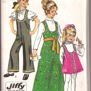 Op de afbeelding: Een vintage Simplicity naaipatroon voor meisjesjurken en overalls. Het patroon bevat drie verschillende stijlen: een groene bloemenjurk met een gele riem, een roze jurk met een witte kraag en een bruine overall met een wit bloesje. Het patroon is gemarkeerd met "Jiffy easy cut - easy sew" en bevat twee hoofdstukken.