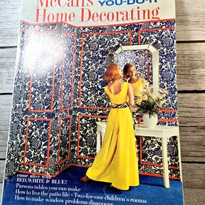 May include: A vintage McCall's Home Decorating magazine cover from Spring-Summer 1969. The cover features a woman in a yellow dress standing in front of a mirror, with a blue and white floral wallpaper behind her. The text on the cover reads "McCall's You-Do-It Home Decorating" and "come alive with RED, WHITE & BLUE!"