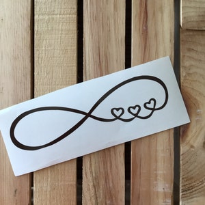 May include: A white vinyl sticker with a black infinity symbol and three small hearts. The hearts are inside the infinity symbol.