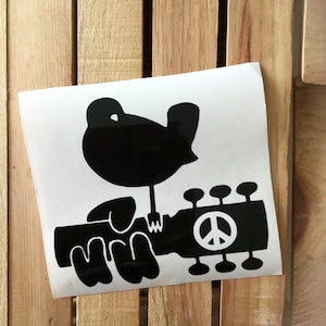 May include: Black and white vinyl sticker of a bird playing a guitar with a peace sign on the guitar.