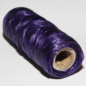 May include: A roll of deep purple satin ribbon, wound tightly around a cardboard core.