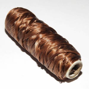 May include: A spool of brown hair extensions. The hair is wrapped tightly around a cardboard tube.