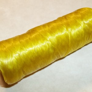 May include: A spool of bright yellow thread, tightly wound and cylindrical in shape. The thread has a slightly shiny, smooth texture, suggesting it's made of a synthetic material. Ideal for sewing, crafting, or other textile projects.