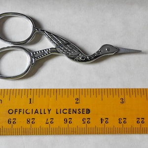 May include: Silver-toned scissors shaped like a bird with a ruler for scale. The scissors are about 3 inches long.