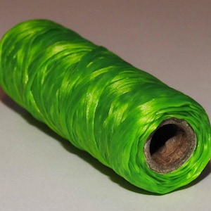 May include: A roll of bright green thread with a shiny finish. The thread is wound tightly around a brown cardboard spool.