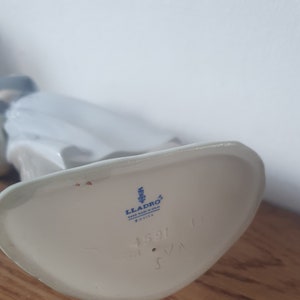 Pode incluir: Figurinha de porcelana branca com um logotipo Lladro azul e branco e o n&uacute;mero 1591 na parte inferior.