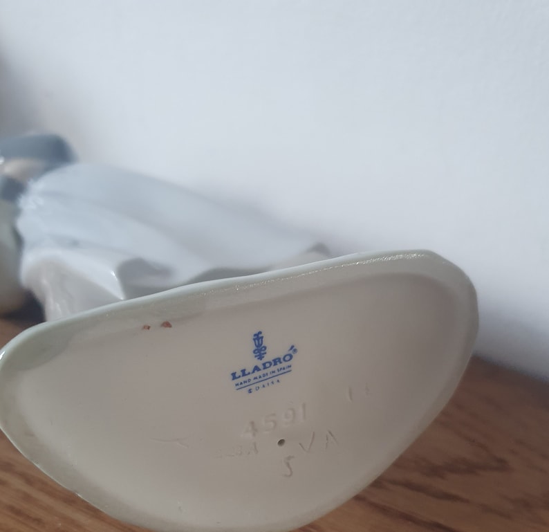 Pode incluir: Figurinha de porcelana branca com um logotipo Lladro azul e branco e o n&uacute;mero 1591 na parte inferior.
