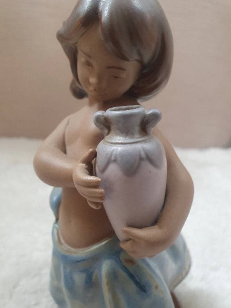 May include: A ceramic figurine of a girl holding a light blue and white pitcher. The girl is wearing a blue and white dress and has brown hair.