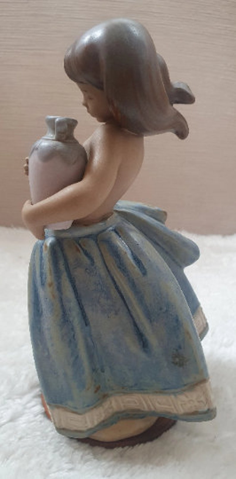 May include: A porcelain figurine of a girl wearing a blue dress and holding a pink and white pitcher.