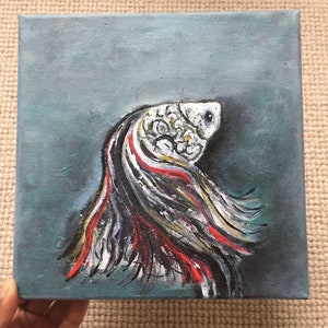 May include: A painting of a white fish with red and black fins against a teal background.