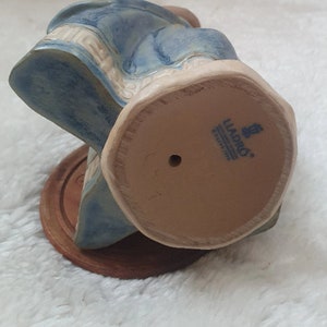May include: A blue and white ceramic figurine of a woman sitting on a chair. The figurine is made by Lladro and has a number 6011 on the bottom.