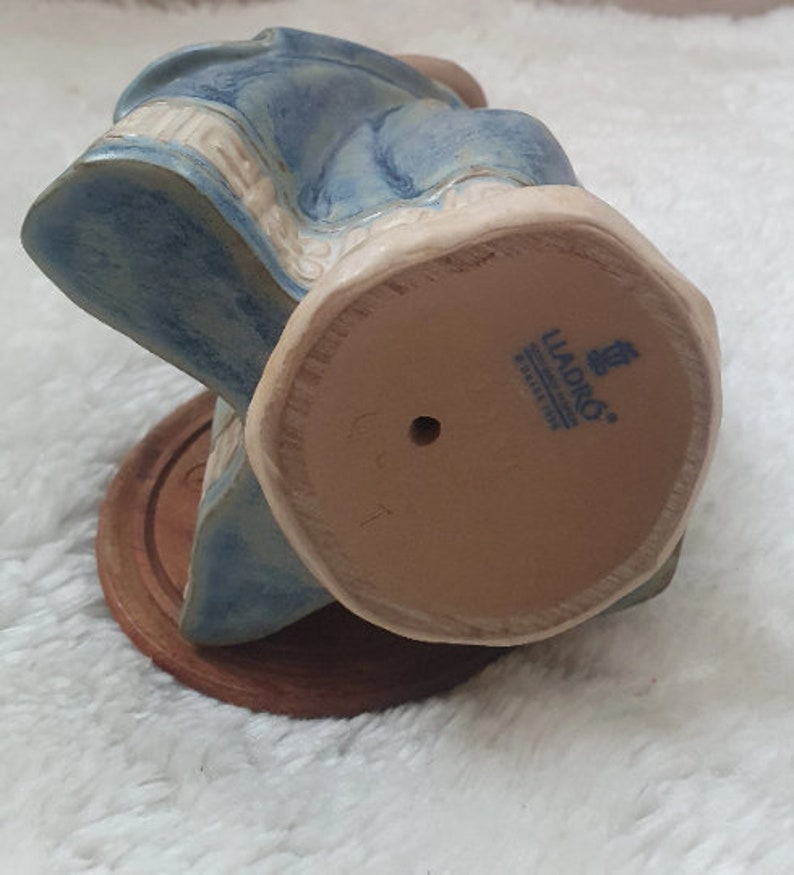 May include: A blue and white ceramic figurine of a woman sitting on a chair. The figurine is made by Lladro and has a number 6011 on the bottom.