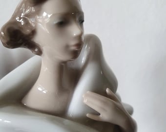 May include: A porcelain figurine of a woman, with brown hair and a serene expression. She is draped in a white garment, with her hands gently posed. The figurine has a smooth, glossy finish and is set against a plain background.
