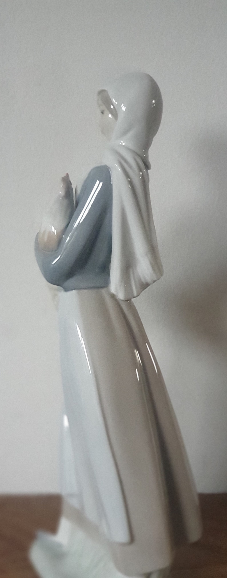 Pode incluir: Uma figura de porcelana de uma mulher vestindo um manto branco com capuz e um vestido azul, segurando um pequeno p&aacute;ssaro branco em seus bra&ccedil;os.
