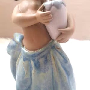 May include: A porcelain figurine of a young girl wearing a blue and white dress, holding a white and blue ceramic pitcher.