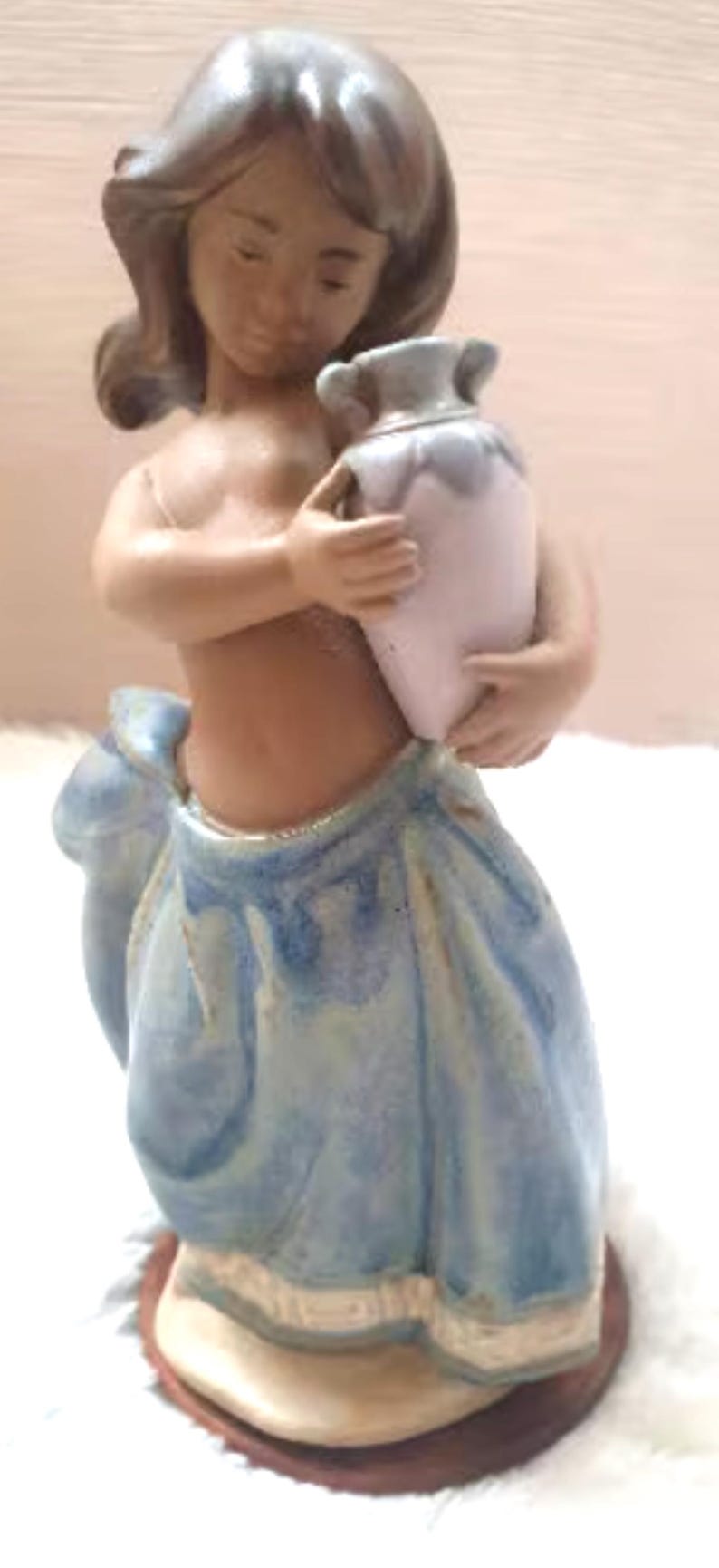 May include: A porcelain figurine of a young girl wearing a blue and white dress, holding a white and blue ceramic pitcher.