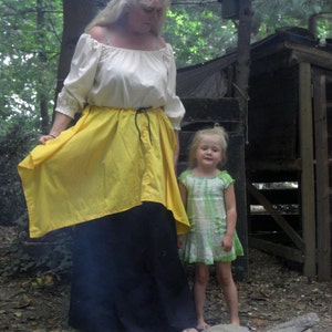 May include: A woman in a cream off-the-shoulder blouse, a yellow skirt, and a long black skirt. A young girl in a green and white dress stands nearby. The image is set outdoors with the text "Brown's Thread Works" at the bottom.