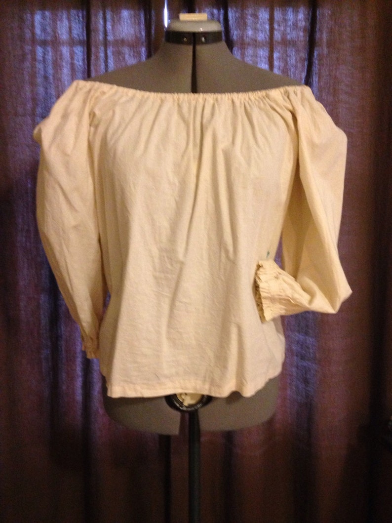 May include: Cream-coloured off-the-shoulder blouse with long sleeves. The blouse is made of a soft, slightly textured fabric. The sleeves have a gathered detail at the cuffs. The blouse is displayed on a mannequin.