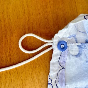 May include: Close-up of a drawstring bag with a blue floral pattern. A white drawstring is looped through the fabric and secured with a blue button. The bag is on a wooden surface.